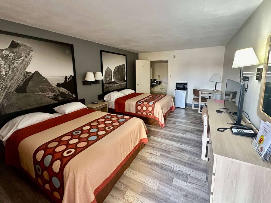 A hotel room with two beds, a desk with a computer, a chair, and a desk lamp.