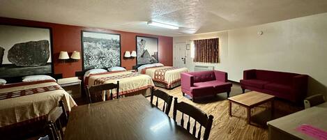 A room with two beds, a wooden dining table, a red sofa, and a small table.