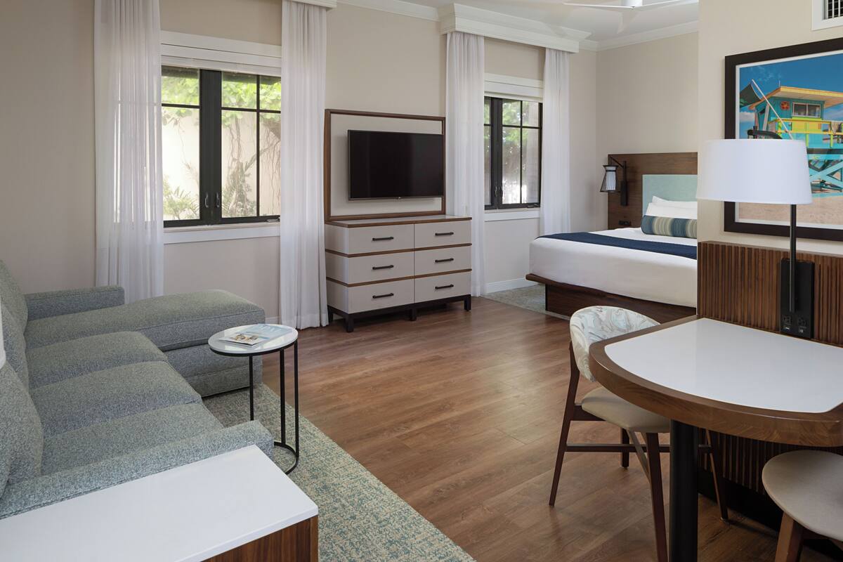 Una habitación de hotel con sofá, cama, televisor, una mesita y una silla.