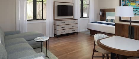 A hotel room with a sofa, a bed, a TV, a small table, and a chair.