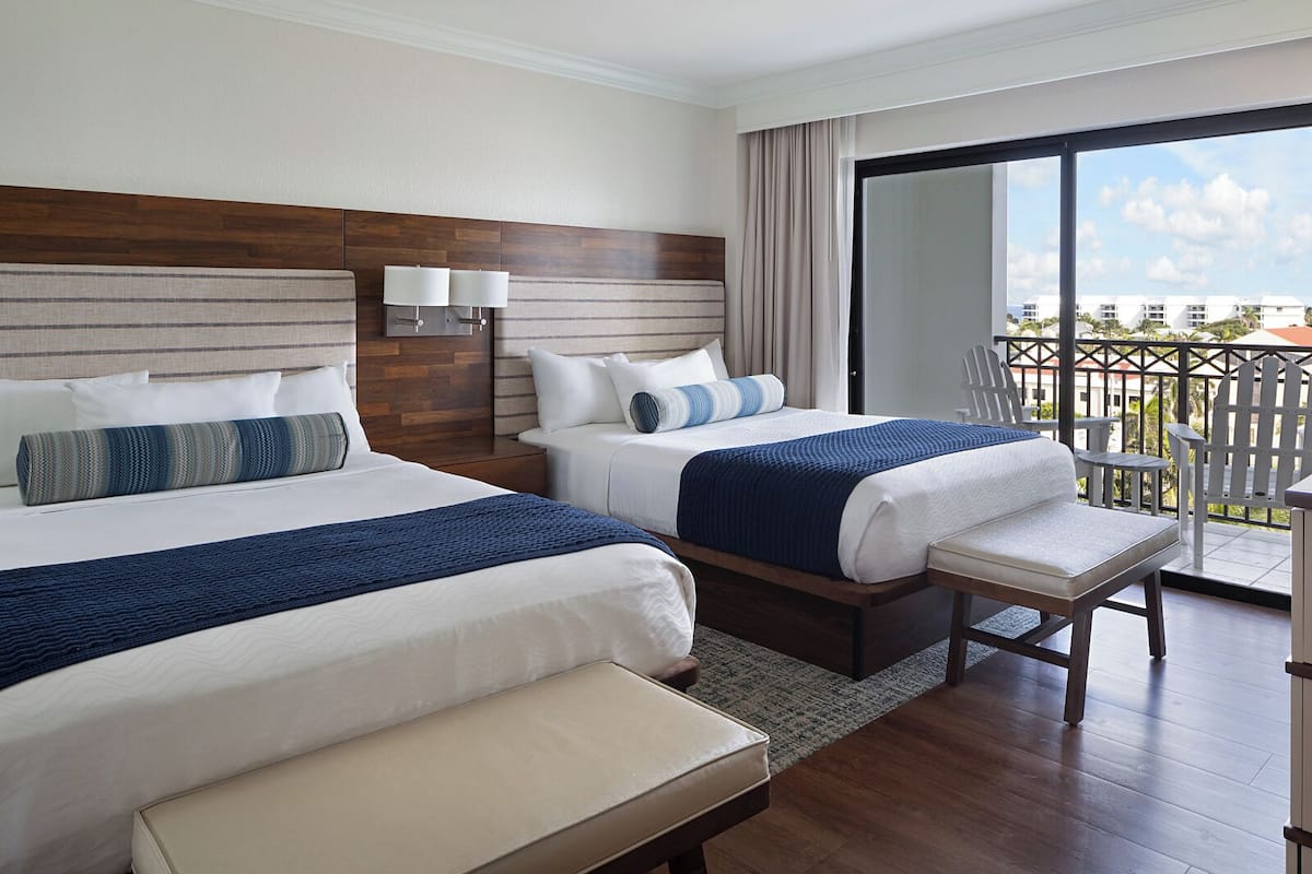 Habitación de hotel con dos camas, un balcón y vistas a edificios.