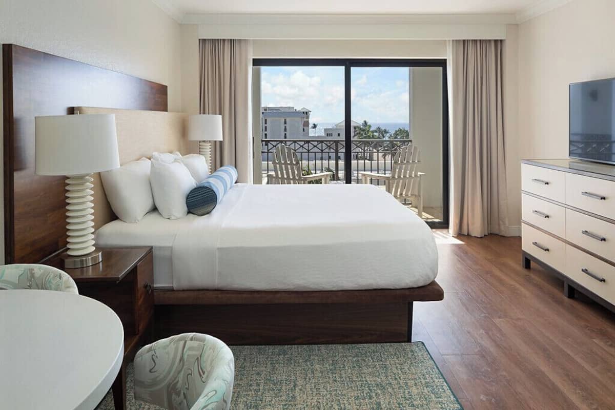 Habitación de hotel con una cama grande, televisión, escritorio con lámpara y balcón con sillas.