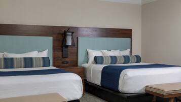 A hotel room with two beds, a nightstand, a lamp, and a small table.