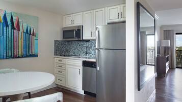 A modern kitchen with white cabinets, stainless steel appliances, and a colorful artwork on the wall.