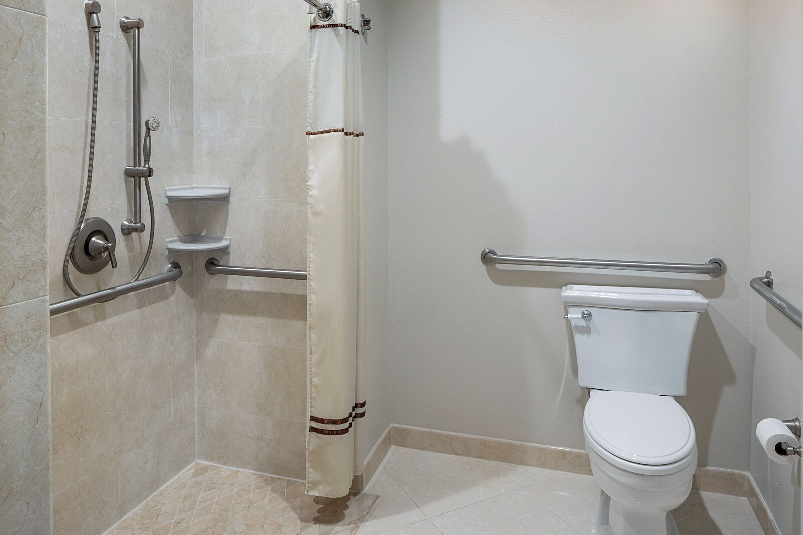 Ein Badezimmer mit Dusche, Toilette, Haltegriffen und einem Handtuchhalter.