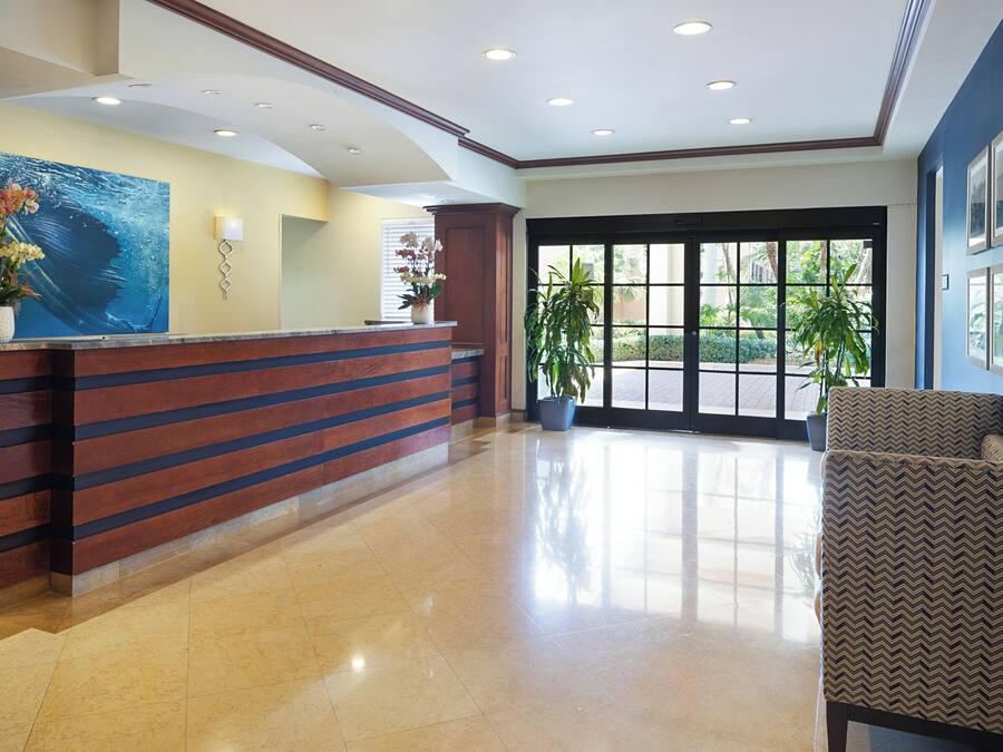 A reception area with a wooden reception desk, a large abstract painting, potted plants, and a seating area with patterned upholstery.