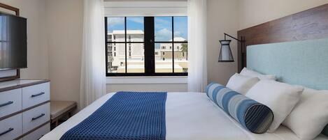 A hotel room with a bed, a TV, a window with a view of buildings, and a lamp.