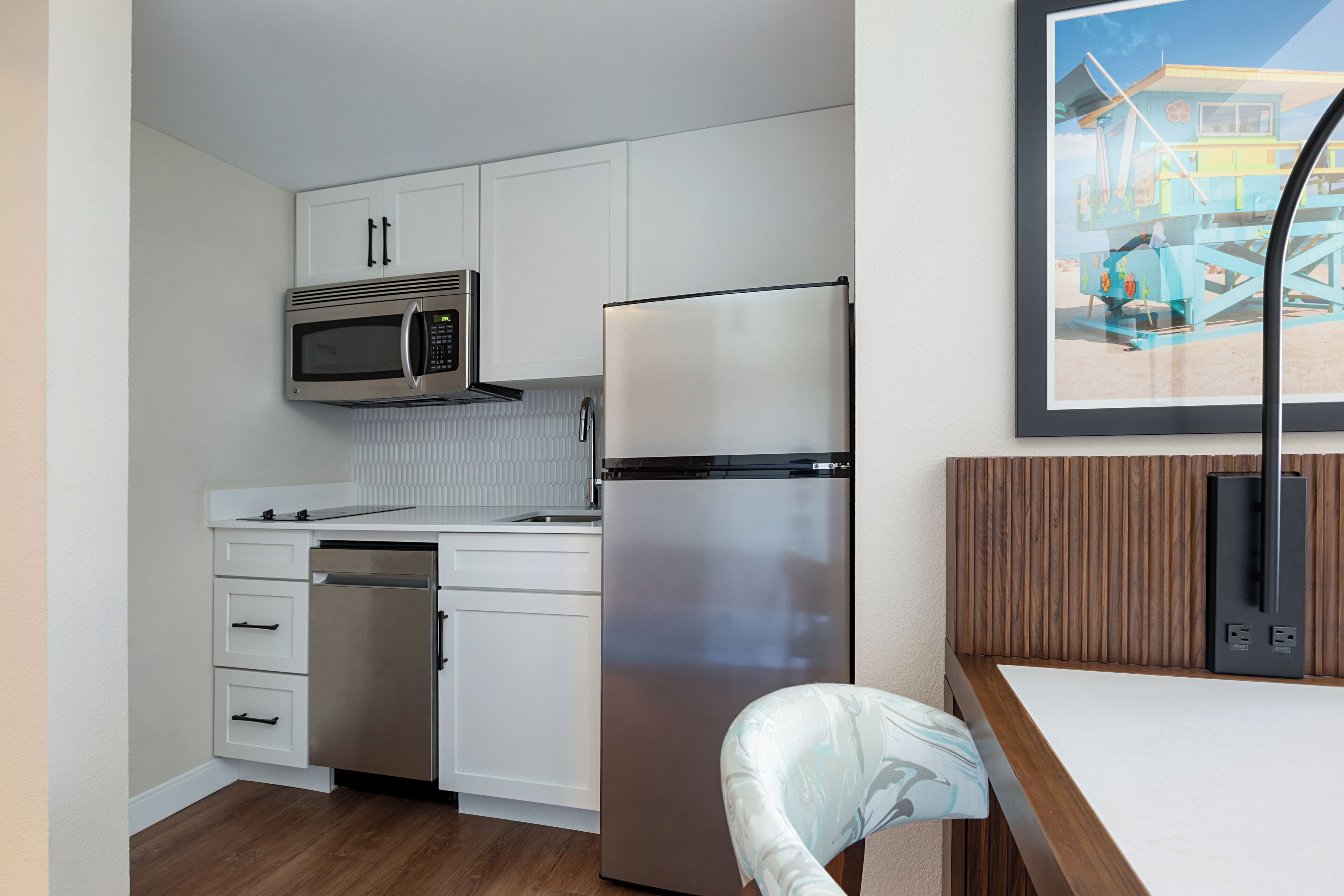 Cocina compacta con armarios blancos, un refrigerador de acero inoxidable, un microondas y una encimera de madera.