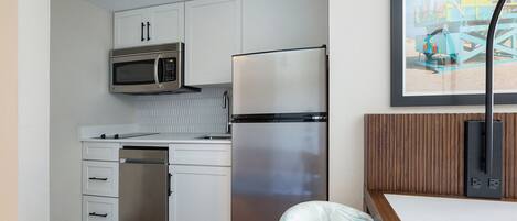 Cocina compacta con armarios blancos, un refrigerador de acero inoxidable, un microondas y una encimera de madera.
