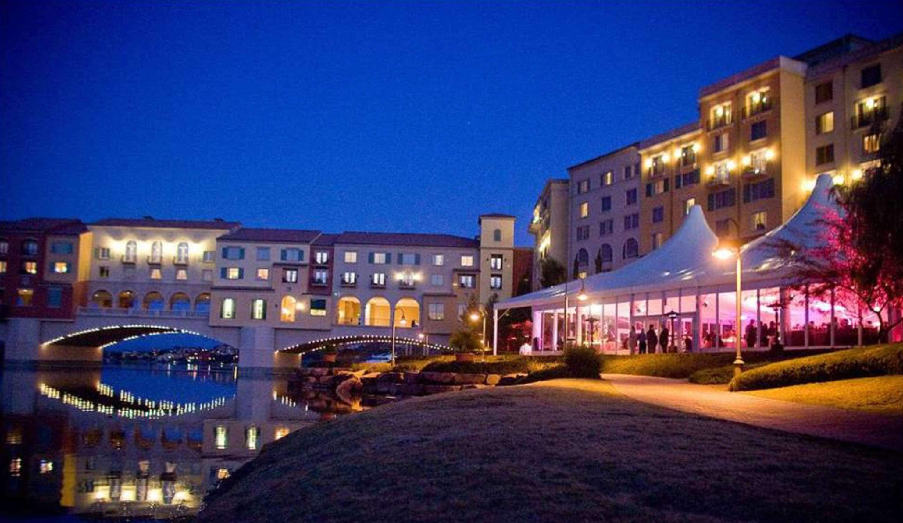 A hotel courtyard at dusk with a reflective pool, a covered seating area, and classical architecture.