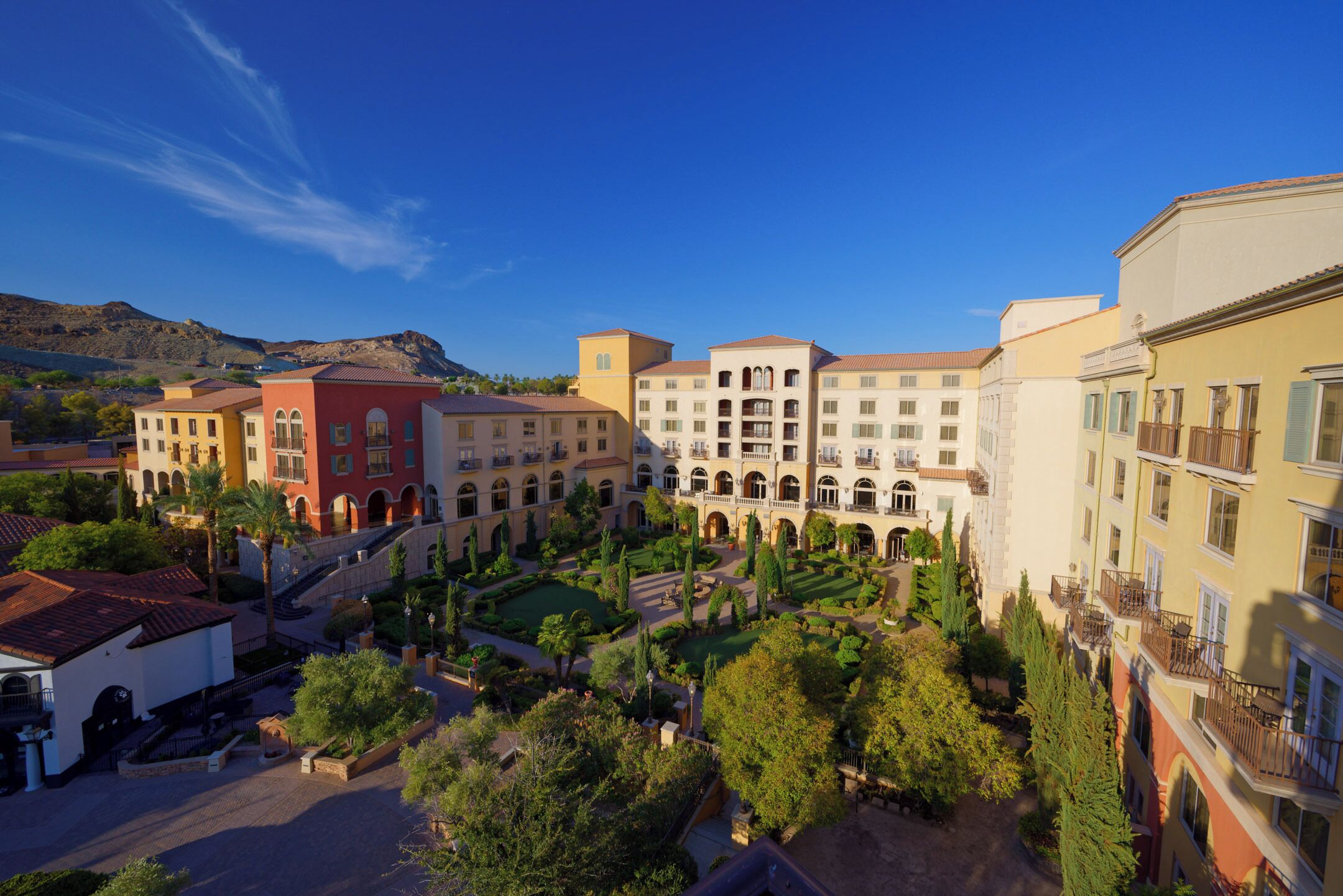 A courtyard with multiple buildings, including a red building with arched windows and a beige building with balconies.