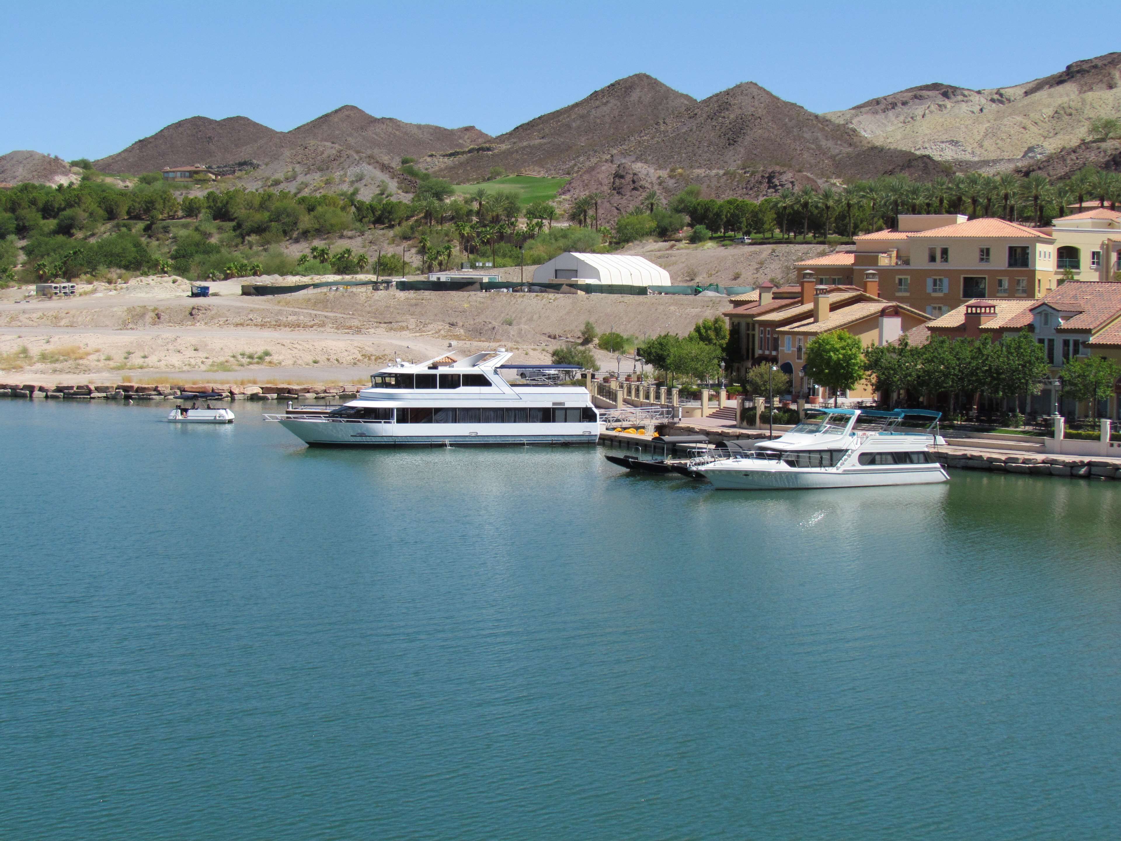 A marina with several boats docked, surrounded by residential buildings and mountains in the background.