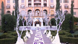 A wedding aisle with white draped trees and a purple floral carpet leading to a building with balconies. - Hilton Lake Las Vegas Resort and Spa (Henderson)