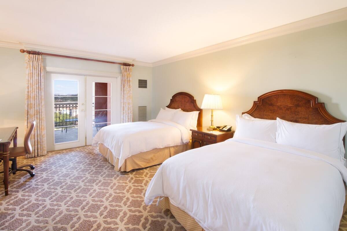 Een hotelkamer met twee bedden, een bureau en een stoel. Er is een balkon met uitzicht.