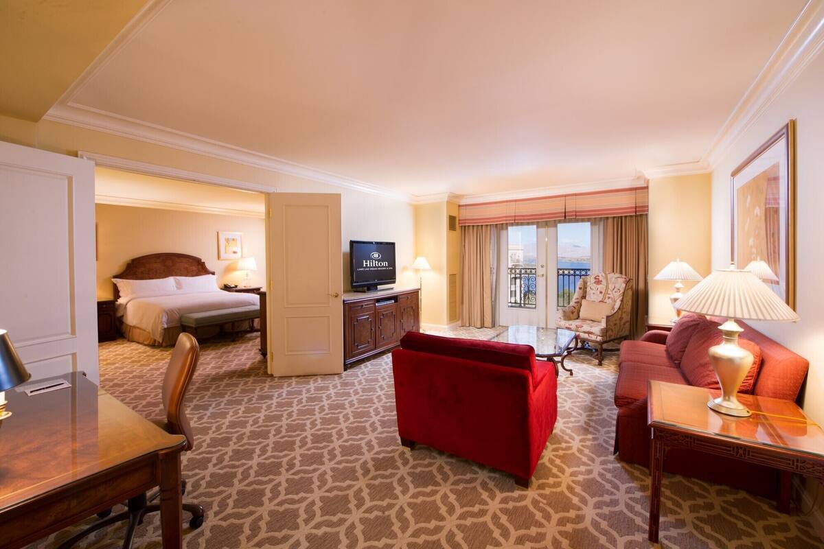 Een hotelkamer met een bed, een televisie, een rode bank, een bureau en een balkon met gordijnen.