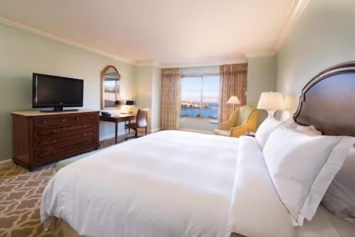 Een hotelkamer met een bed, een televisie, een bureau en uitzicht op zee.