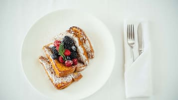 A plate of French toast with berries and powdered sugar, accompanied by a fork and knife on a napkin.