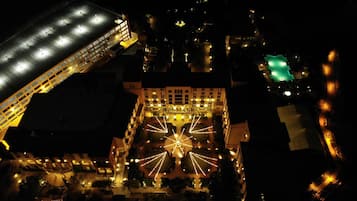 Una vista aerea di un hotel con un cortile centrale illuminato da luci a tenda, circondato da edifici con balconi e una struttura verdeggiante a destra.