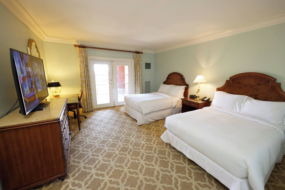 Een hotelkamer met twee bedden, een bureau met een lamp, een televisie en een kamerbreed tapijt met een patroon.