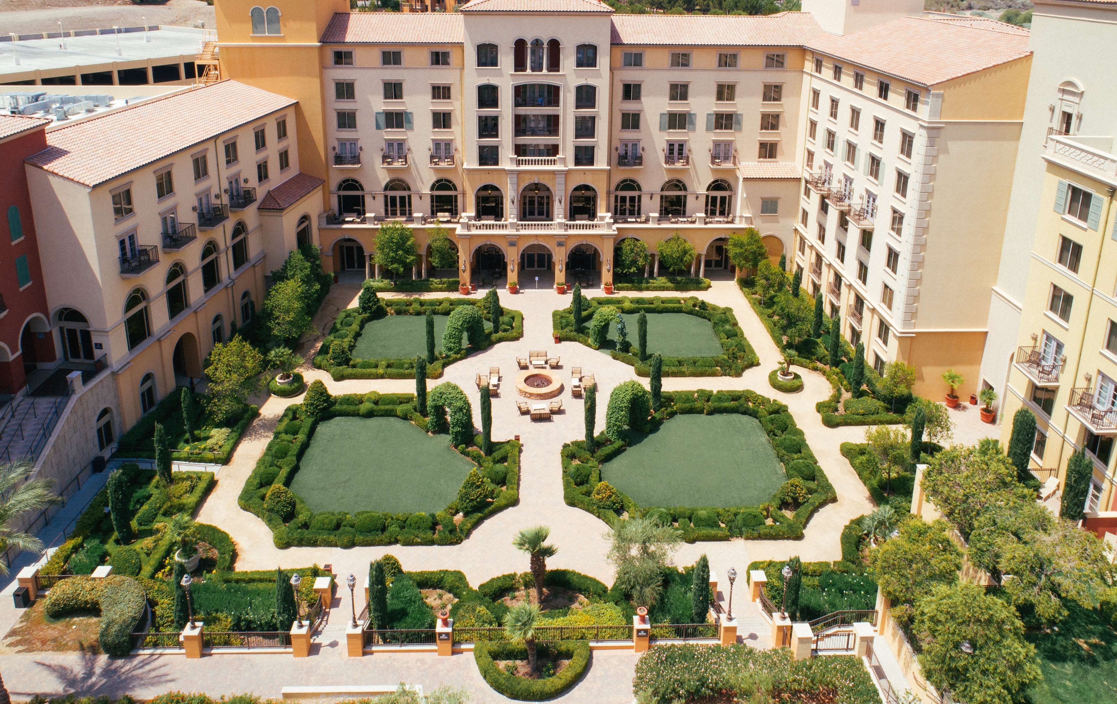 A courtyard with a central fountain, surrounded by manicured gardens and multi-story buildings with balconies.