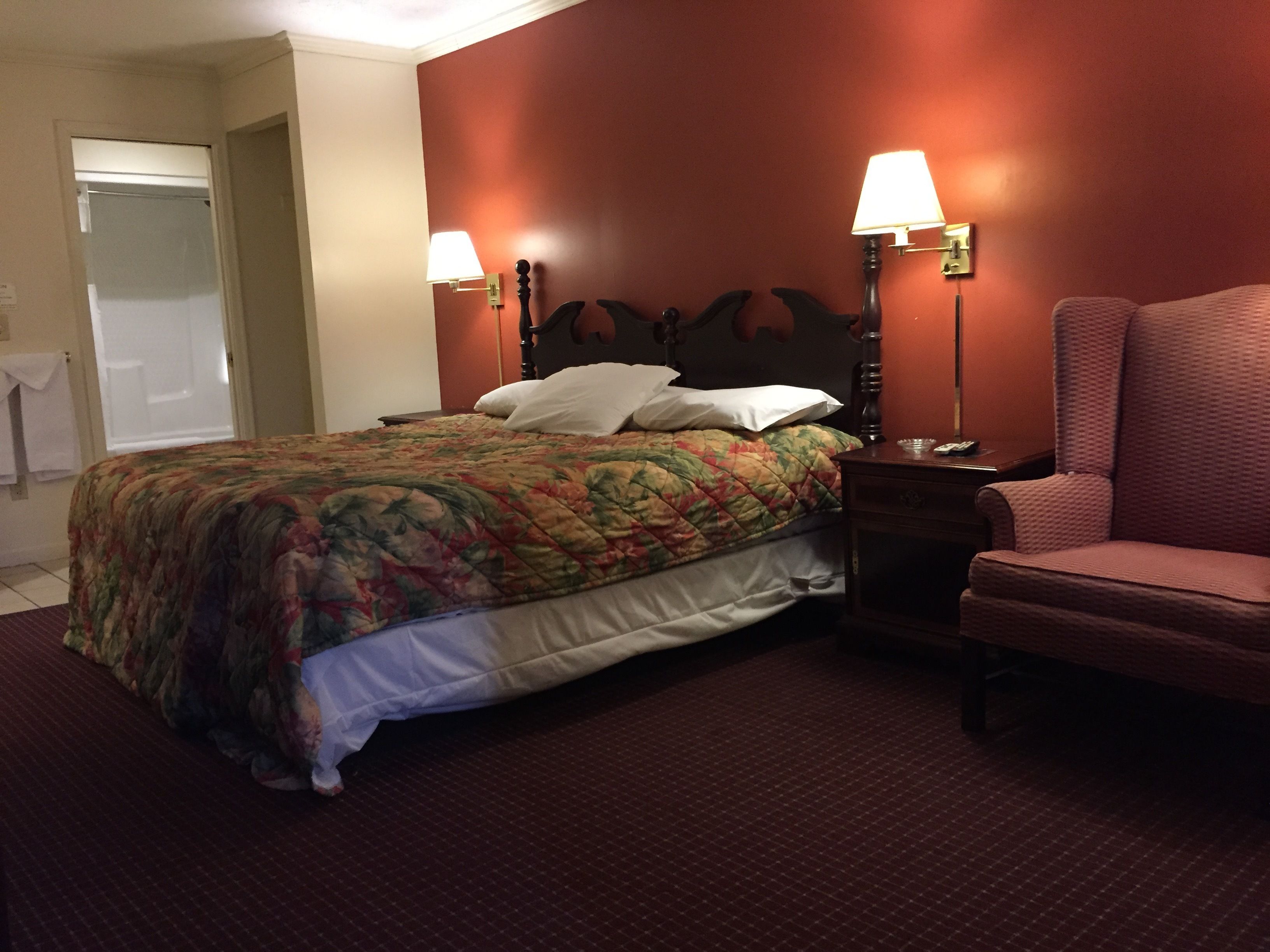 A hotel room with a bed, two bedside lamps, a chair, and a door.