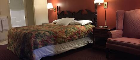 A hotel room with a bed, two bedside lamps, a chair, and a door.