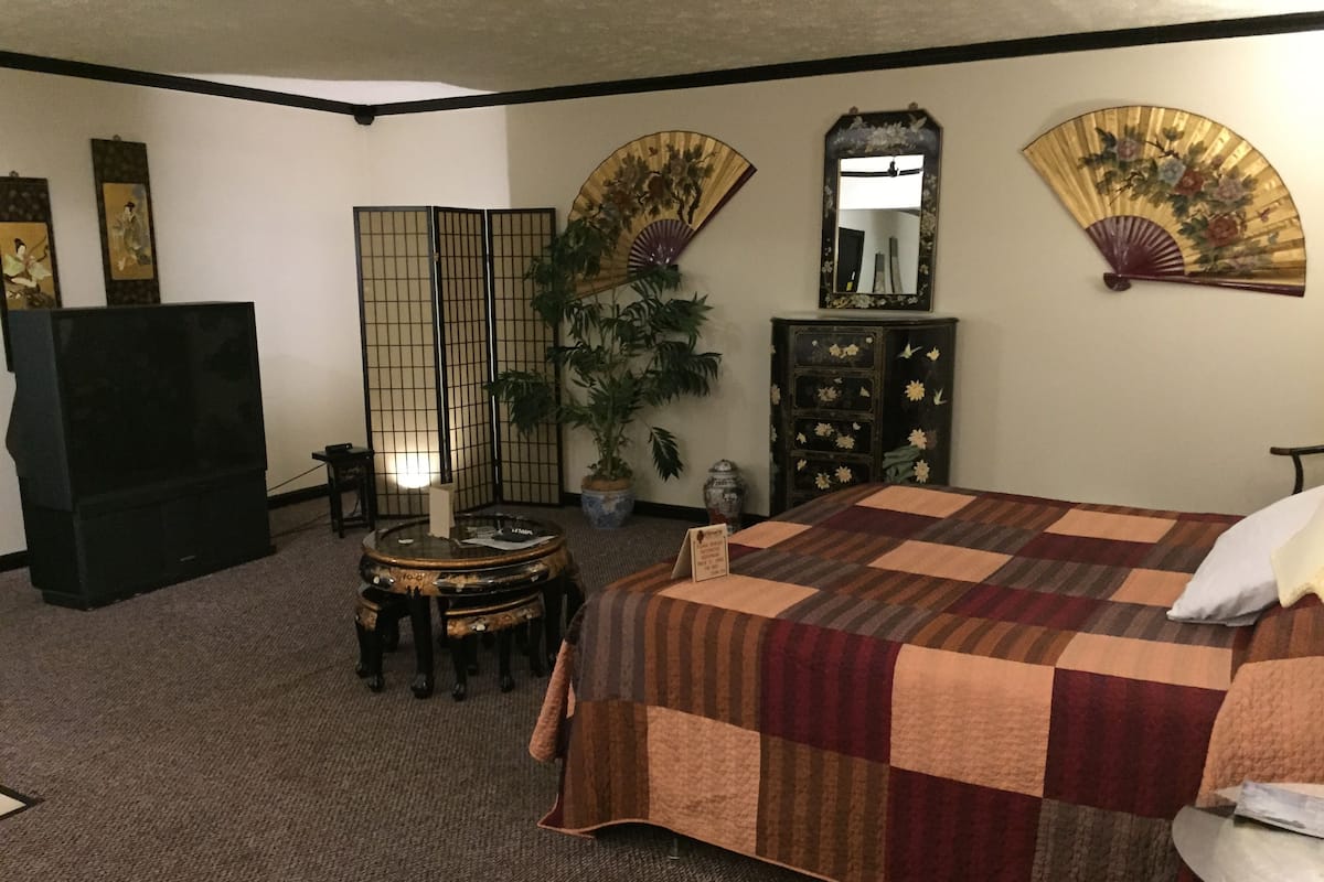 A hotel room with a bed, a desk, a TV, a plant, and traditional decor.