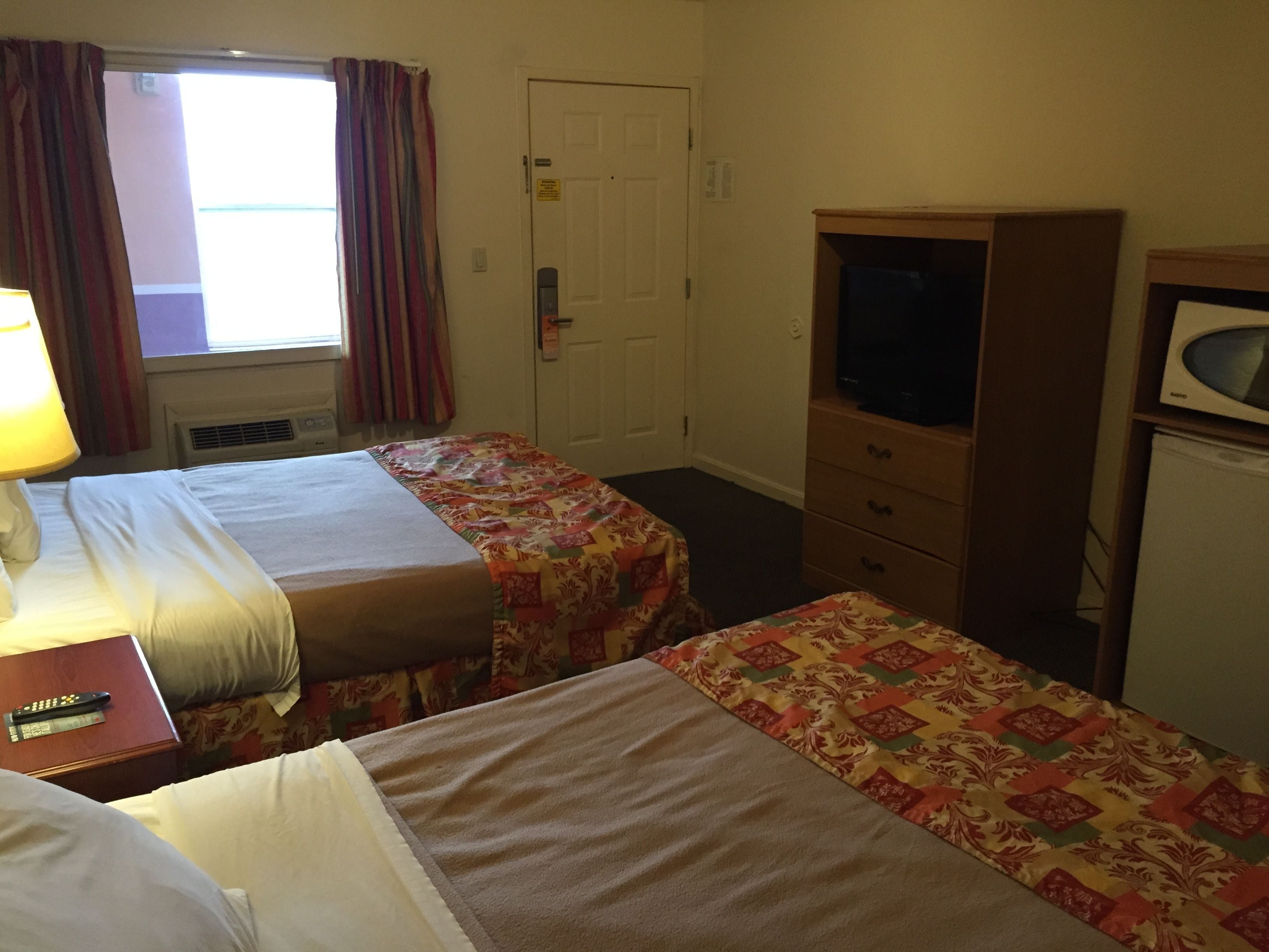 Habitación de hotel con dos camas, televisor, cómoda y ventana con cortinas.