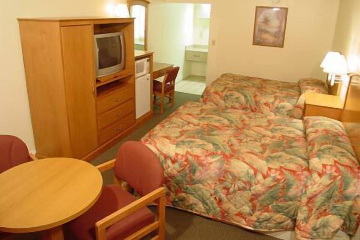 A compact hotel room with a single bed, a small desk, a television, and a chair.