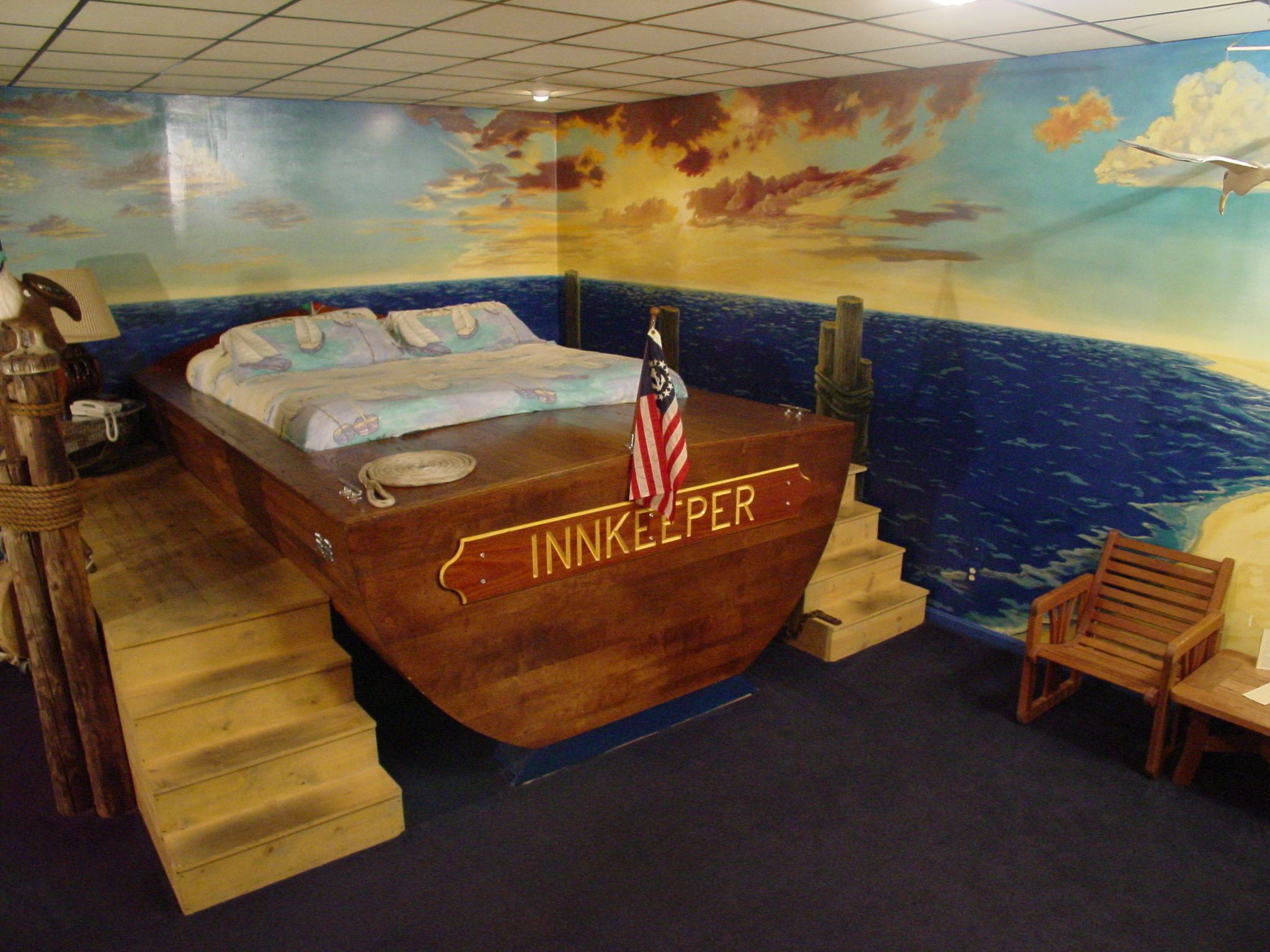 Una habitación con una cama que tiene la etiqueta 'INNKEEPER' y un mural de un barco en la pared.
