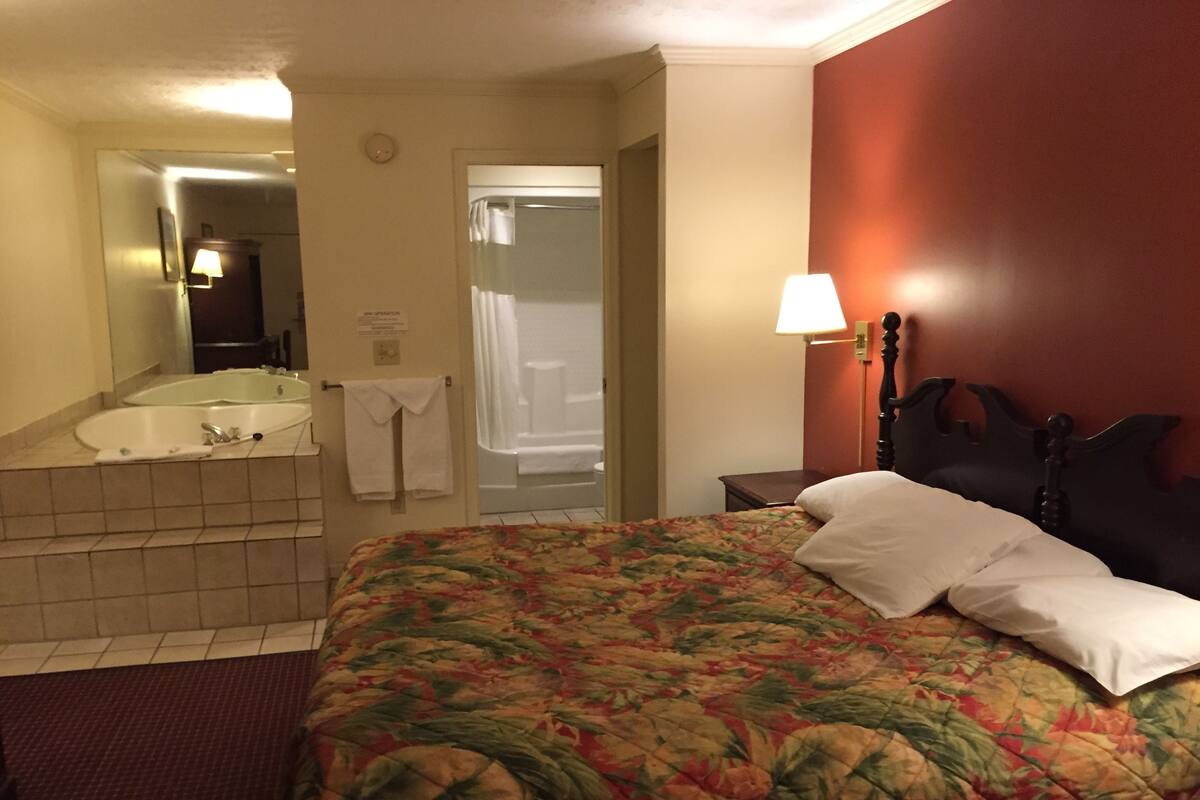 A hotel room with a bed, a bathroom with a bathtub, and a mirror.