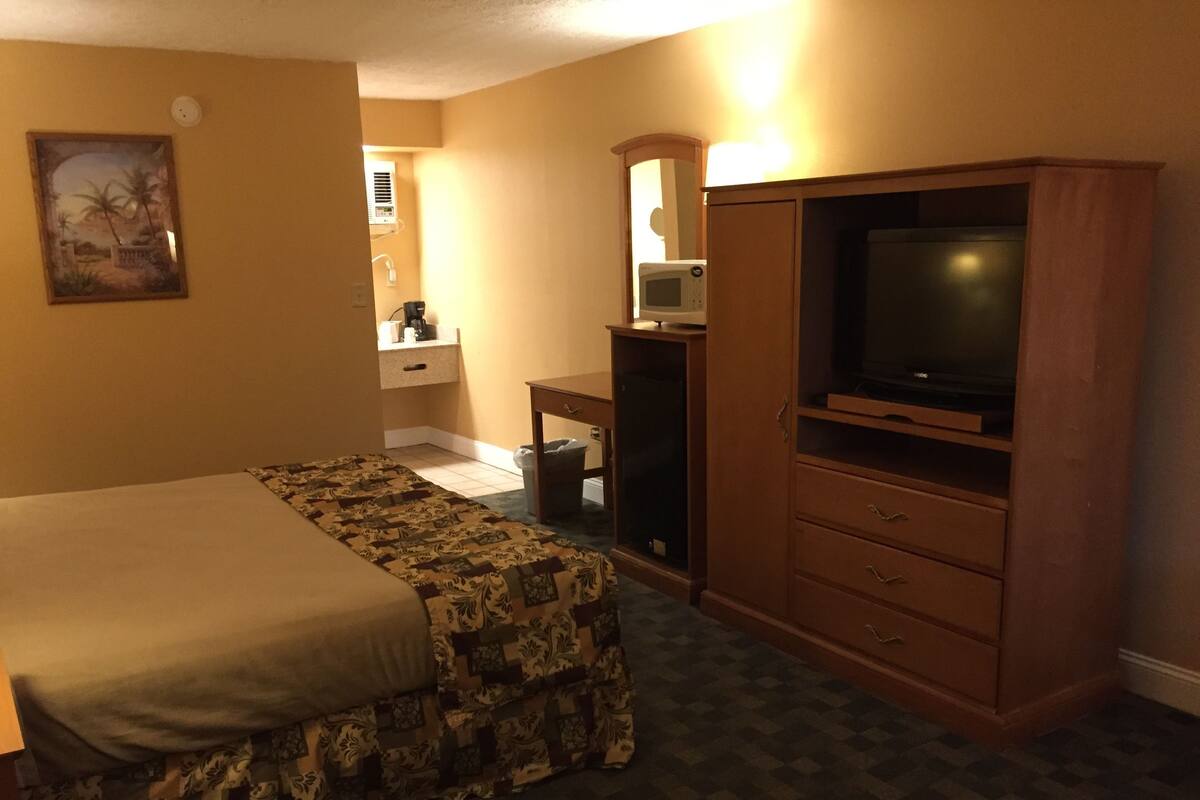 A hotel room with a bed, a desk, a television, and a bathroom visible in the background.