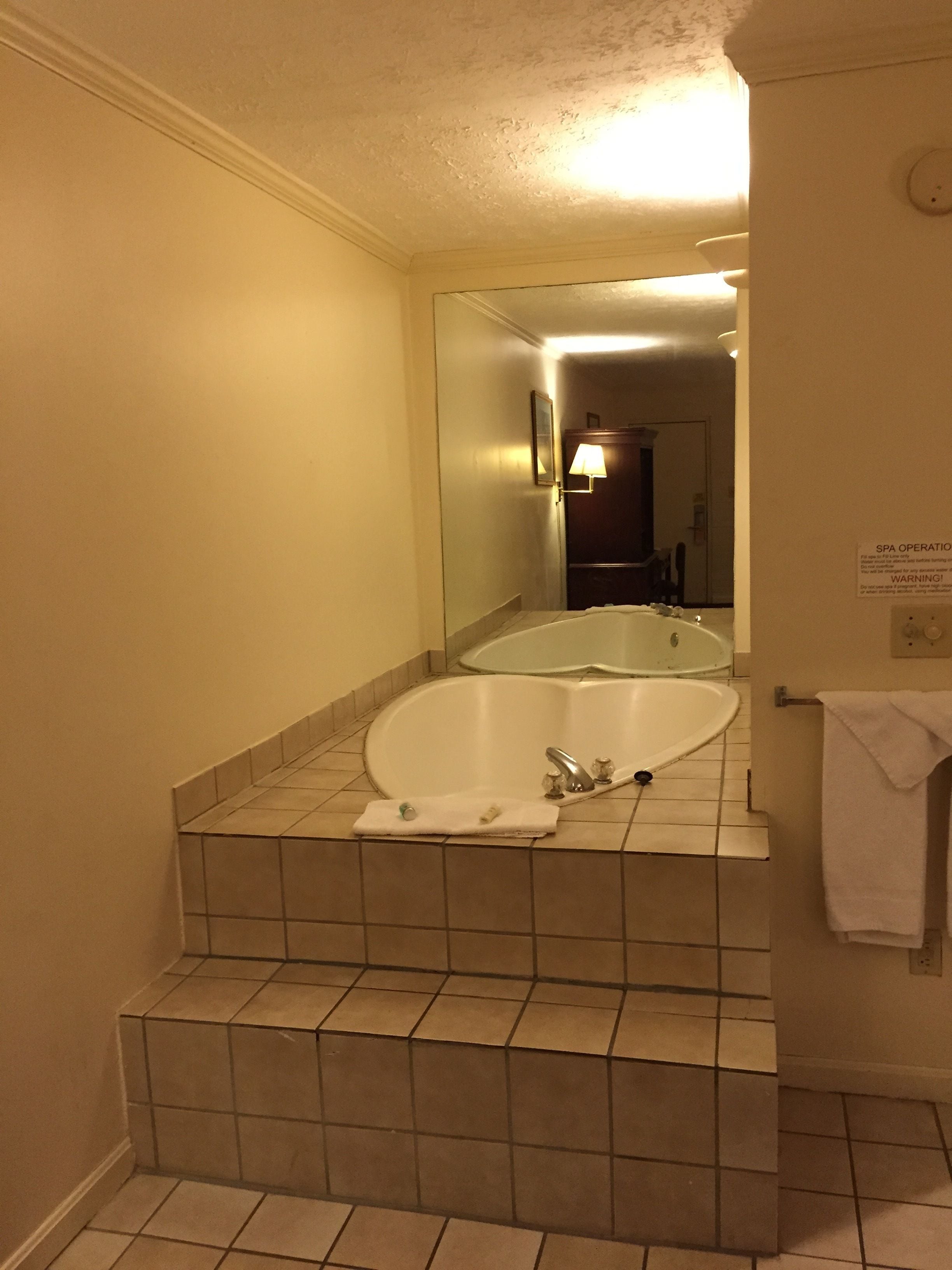 Un baño con una bañera grande, un lavamanos y un espejo. Hay un perchero y un cartel en la pared.