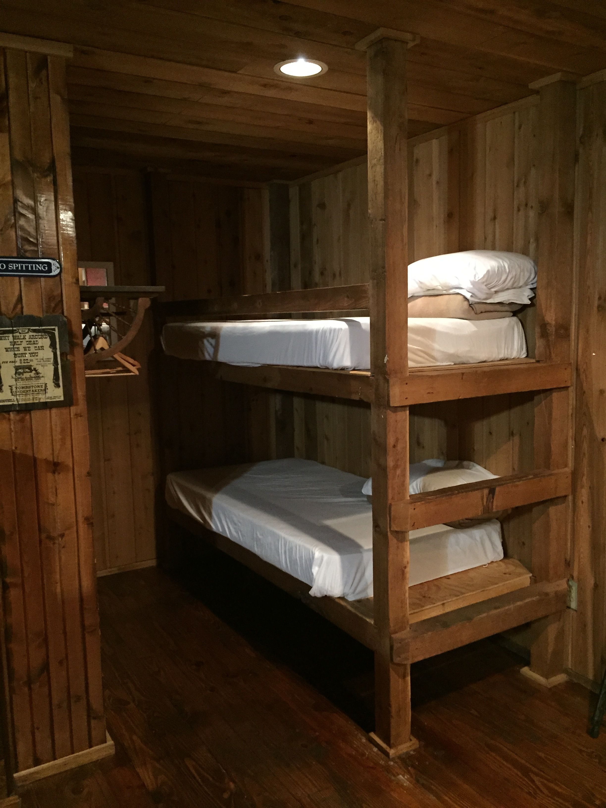 A bunk bed with three levels, wooden walls, and a small shelf with items.