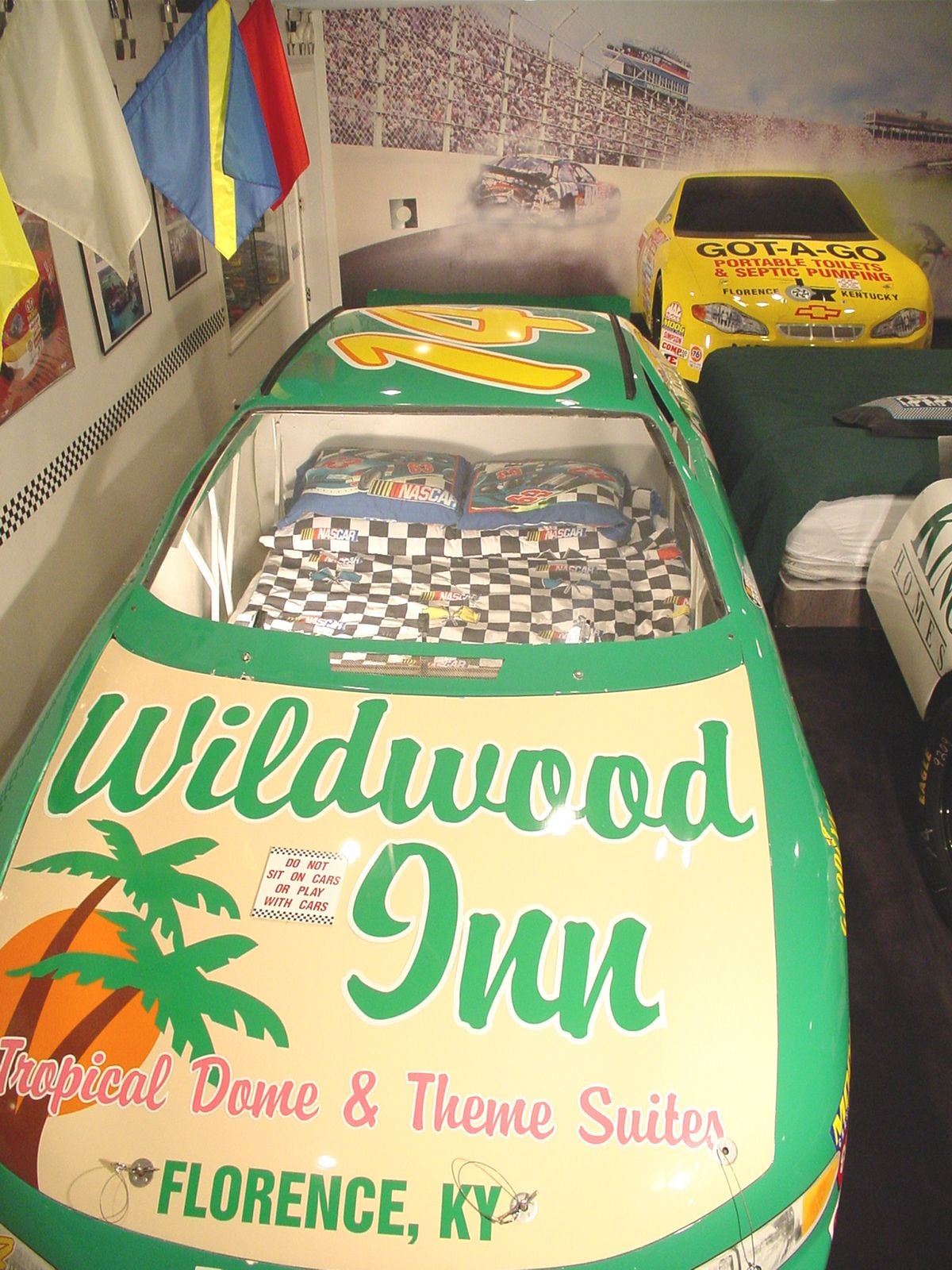 A room with a green racing car bed, a NASCAR bedspread, and a poster of a racing car.