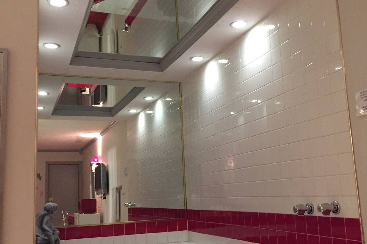 A bathroom with a red bathtub, a large mirror, and white tiled walls.