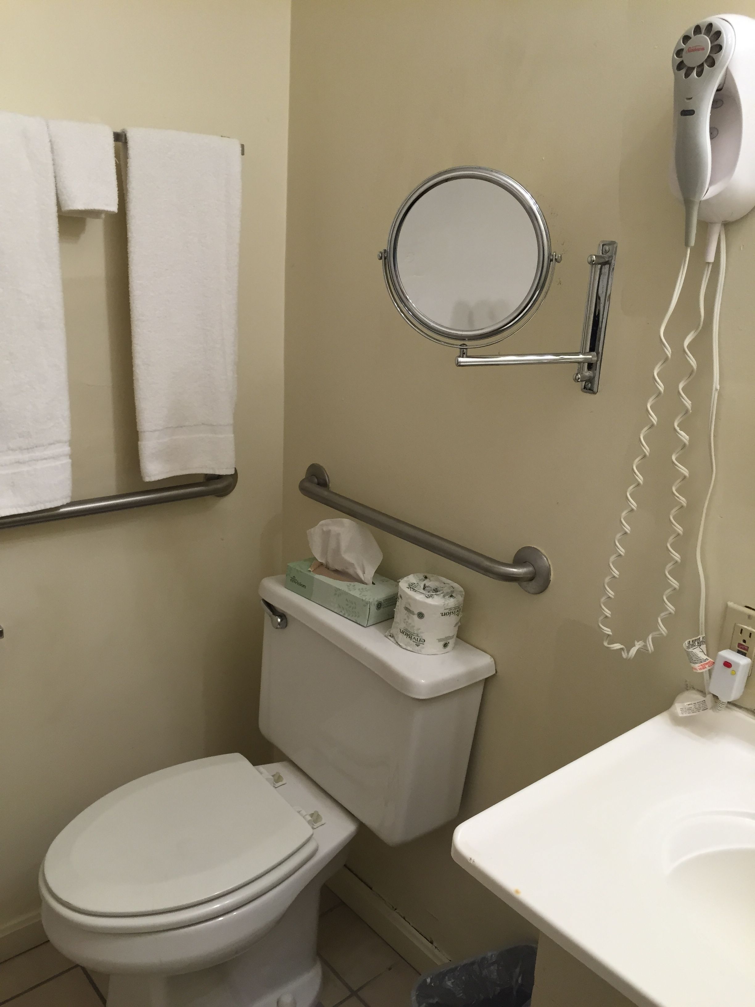Un baño con inodoro, secamanos, espejo y barra para toallas.
