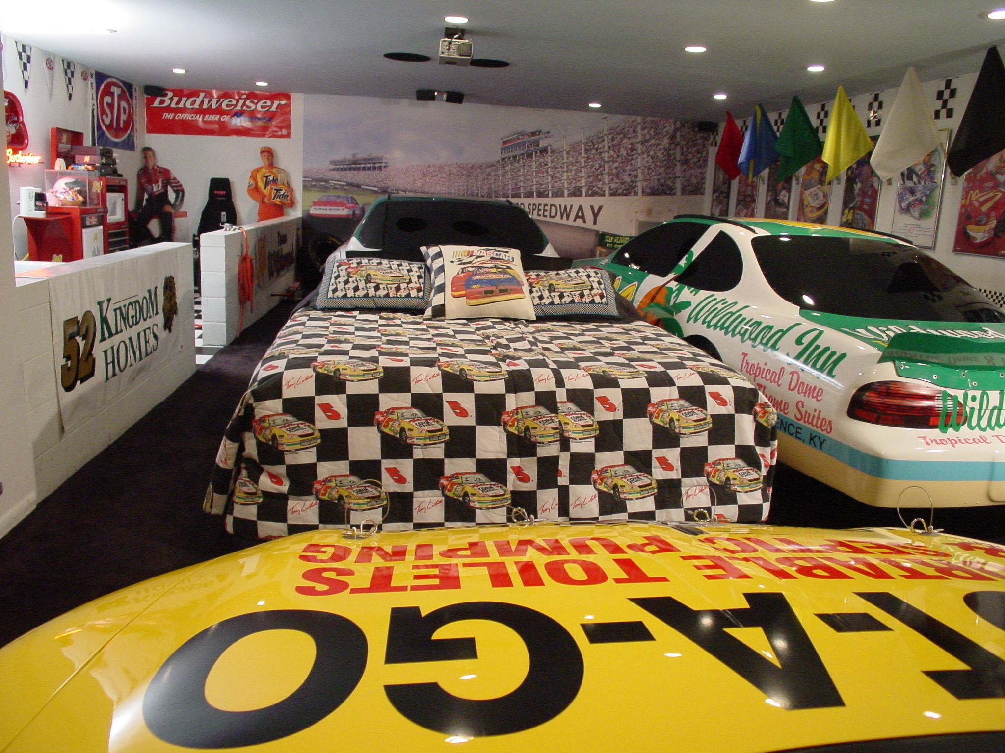 Ein hotelzimmer im Rennfahrer-Stil mit karierter Rennbettwäsche, einem Rennwagen-Modell und verschiedenen Rennsport-Erinnerungsstücken an den Wänden.