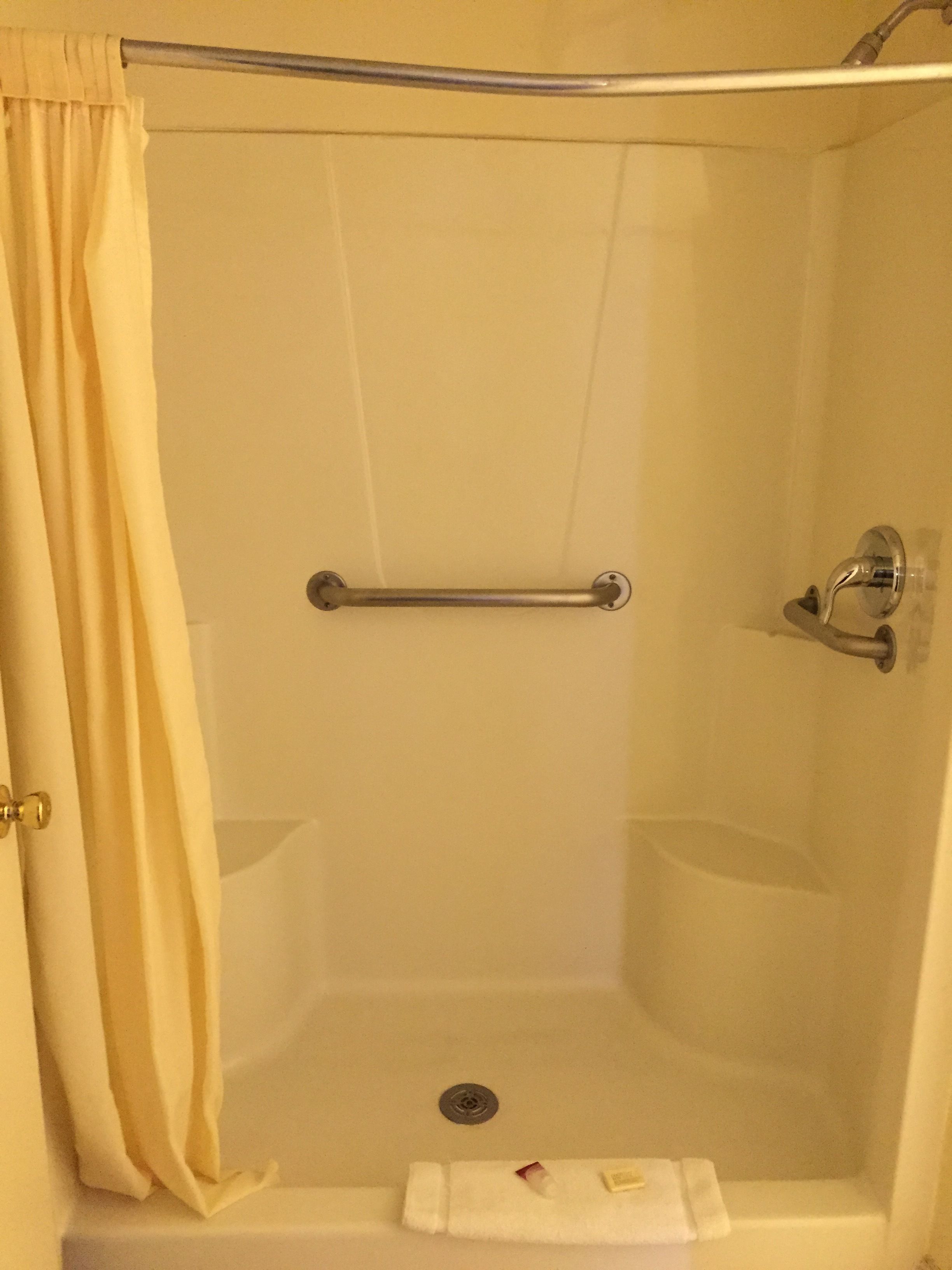 A shower with a grab bar, a towel rack, and a curtain.