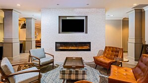 A modern living room with a fireplace, comfortable seating, and a flat-screen TV mounted on the wall. - Radisson Hotel Fairview Heights - St. Louis (Fairview Heights)