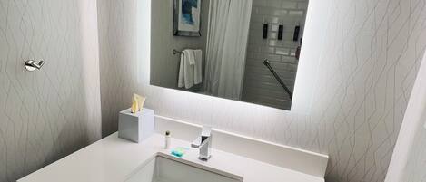 Une salle de bain moderne avec un meuble-lavabo blanc, un grand miroir et un espace douche.