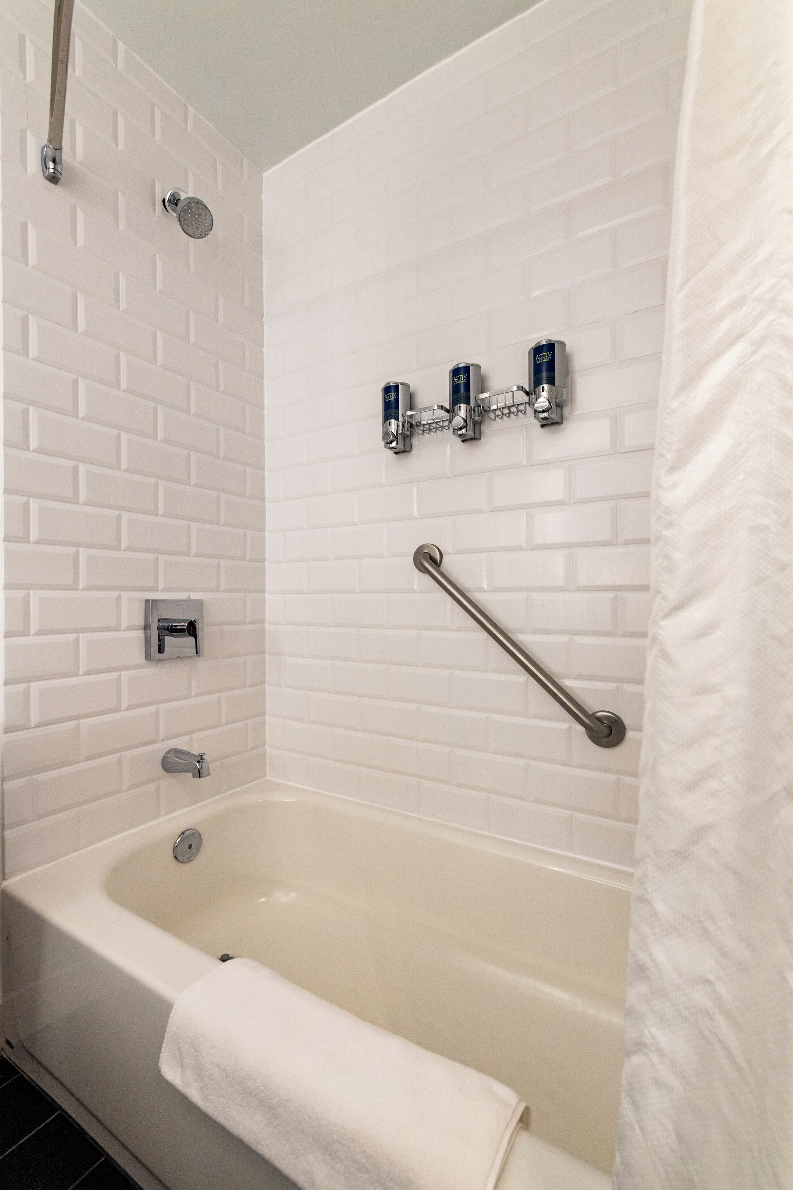 Een badkamer met een witte badkuip, een handdouche, een handdoekrek en een handgreep.