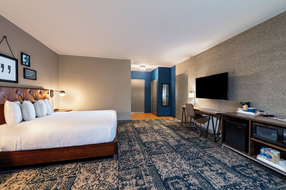 A hotel room with a large bed, a desk, a television, and a microwave.