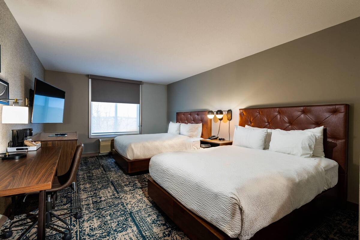 A hotel room with two beds, a desk, a chair, a TV, and a window.