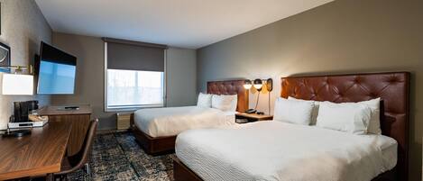 A hotel room with two beds, a desk, a chair, a TV, and a window.