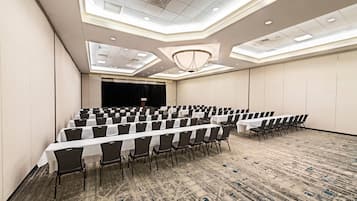 Un salón de conferencias con filas de mesas y sillas, un escenario y un techo alto con tragaluces.