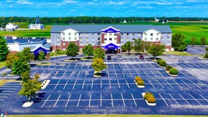A Radisson hotel with a large parking lot, multiple trees, and a green field in the background. - Radisson Hotel Fairview Heights - St. Louis (Fairview Heights)