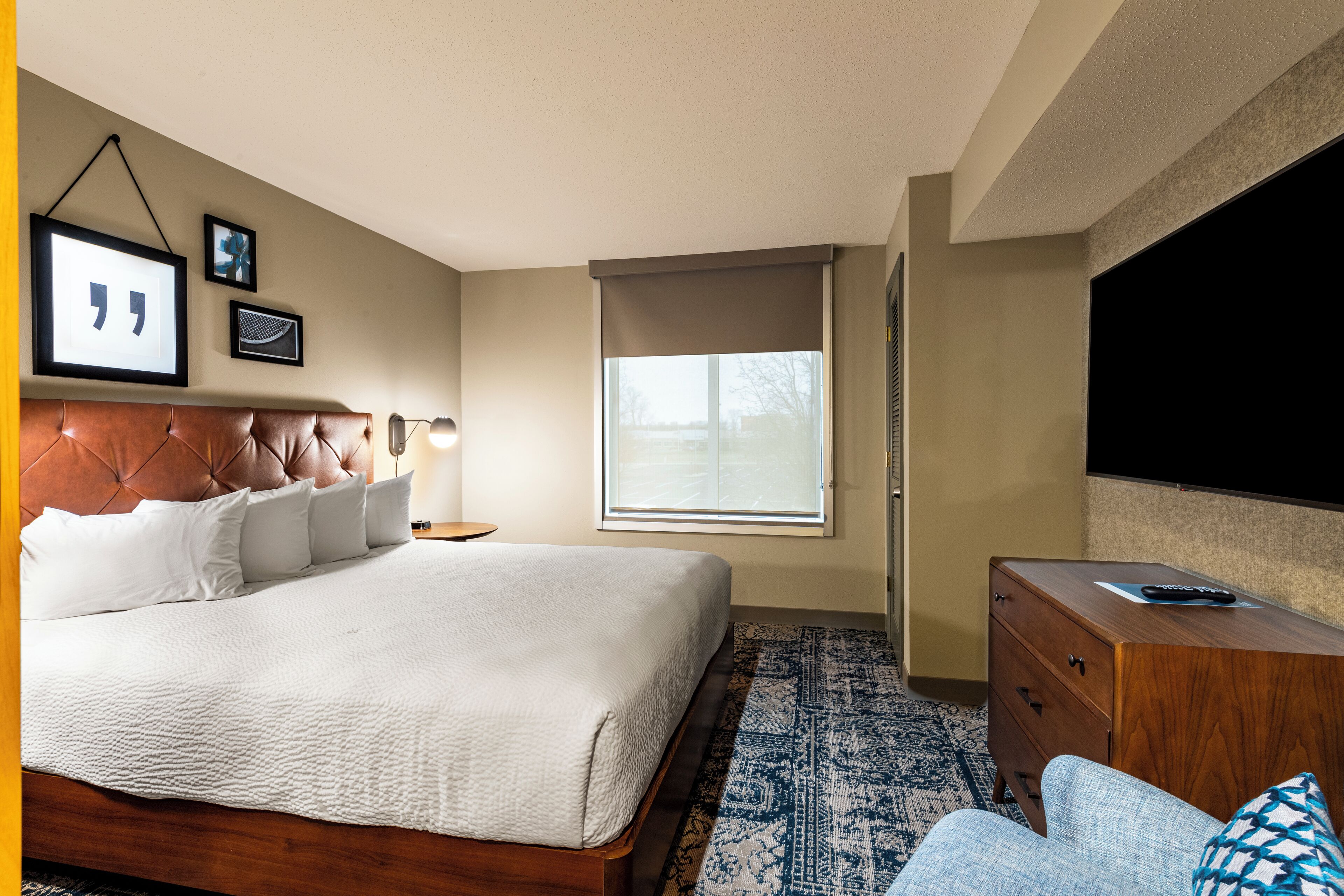 A bedroom with a large bed, a wooden dresser, a television, and a window with blinds.