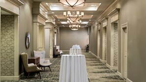 A hotel corridor with a chandelier, a round table with a white tablecloth, and two armchairs. - Radisson Hotel Fairview Heights - St. Louis (Fairview Heights)