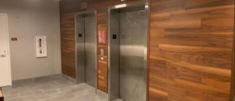A hallway with two elevators, wooden paneling on the walls, and a tiled floor.